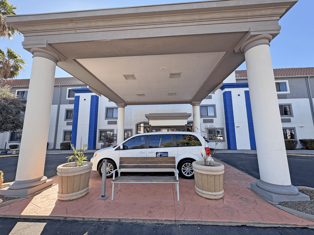 Exterior view of the Holiday Inn Express Tucson Airport, featuring a covered entrance with columns, a parked vehicle, and flower planters.
