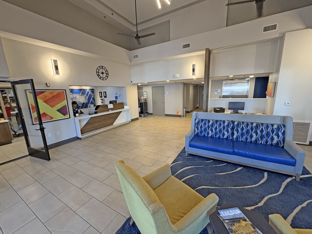 Interior view of the Holiday Inn Express Tucson Airport lobby, featuring a reception desk, seating area with a colorful couch, and modern decor.