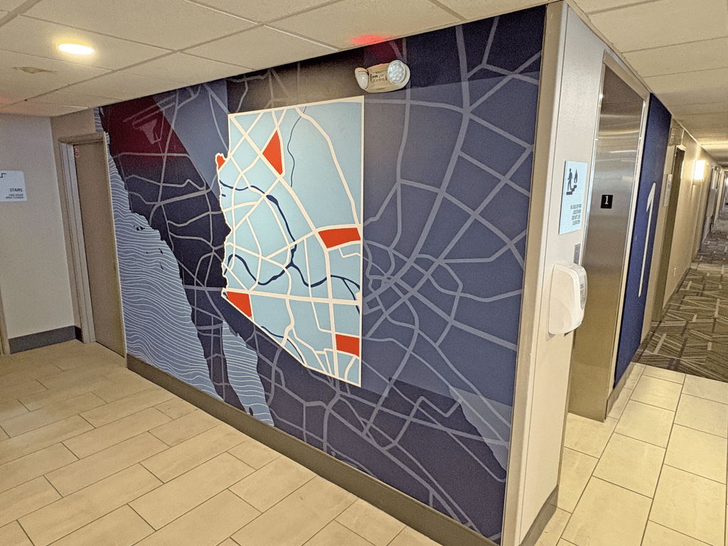 A vibrant wall mural depicting a map of Arizona, with blue and red sections, located in a hotel corridor near the elevators.